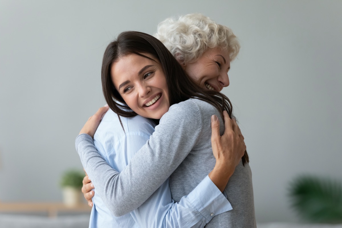 Happy young adult daughter granddaughter visiting embracing hugging old retired grandmother cuddling