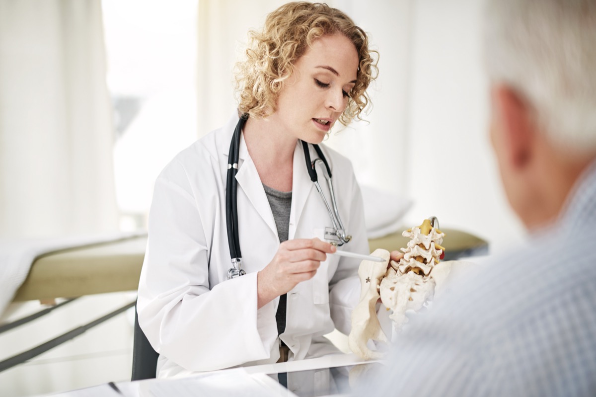 Photo of a doctor explaining a medical procedure with a model to an older patient while sitting in his office