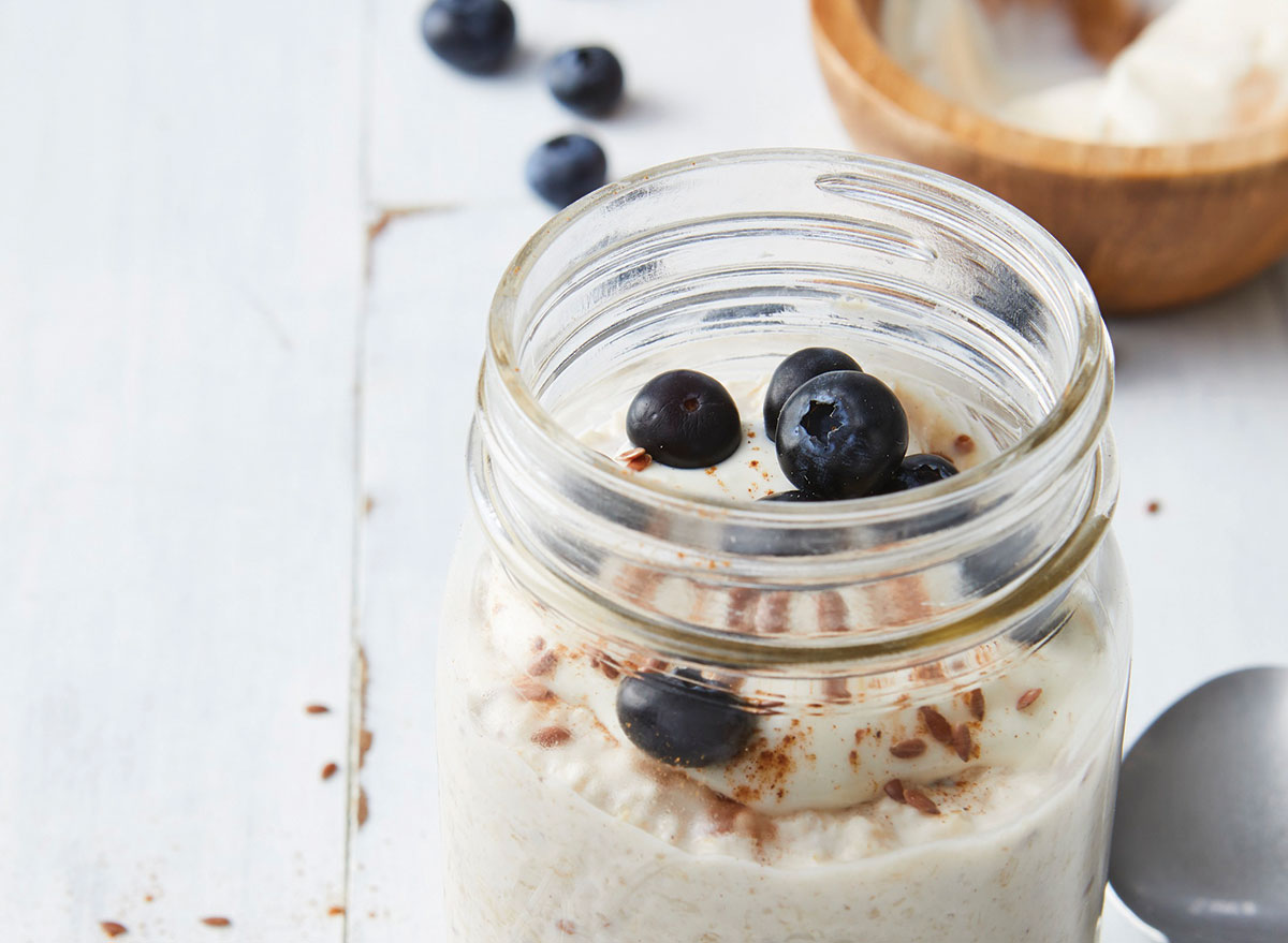 Cinnamon overnight oats roll in open glass mason jar with blueberries on wooden table with spoon