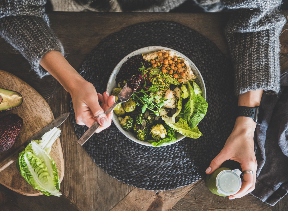 woman holding a smoothie and eating a grain bowl with chickpeas, vegetables, hummus and couscous