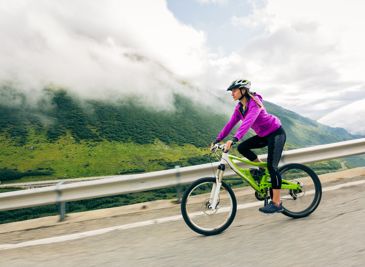 athletic woman rides a bike downhill against a picturesque mountain backdrop