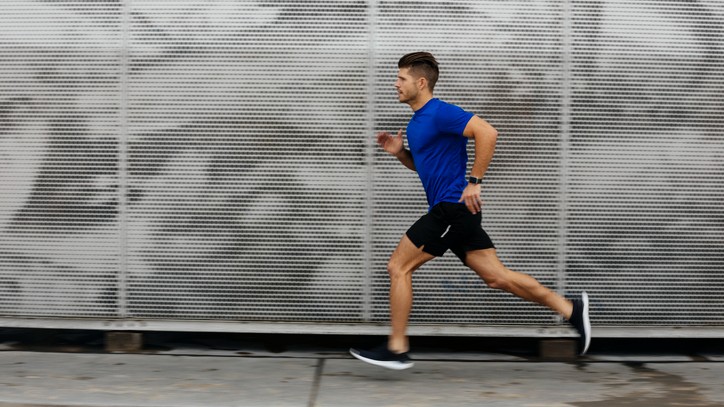 A man in a blue shirt runs past the shutters of some shops that are sprayed with graffiti