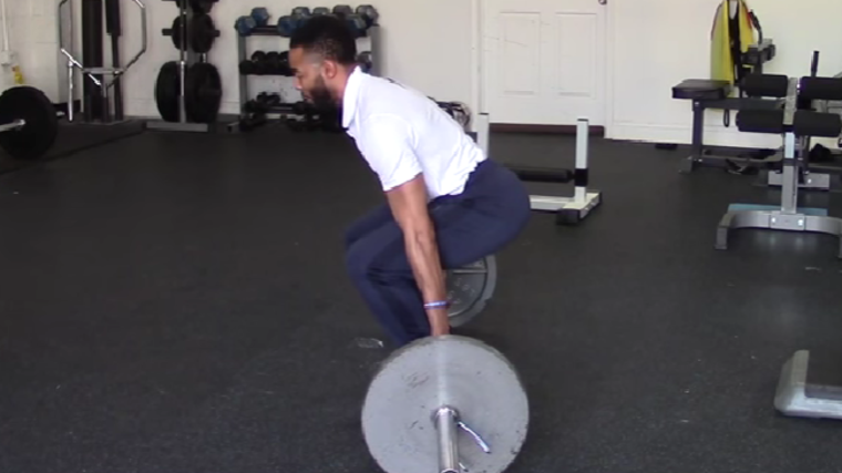 A person wearing a white polo shirt hinges to reach the bar to perform a hack squat.