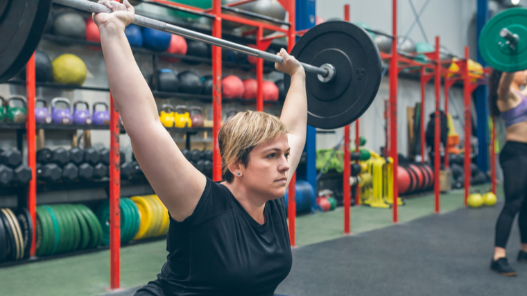 A person performs a barbell snatch in a colorful gym.