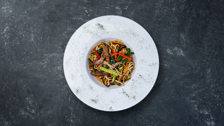 A bowl of noodles filled with vegetables sits on a table.