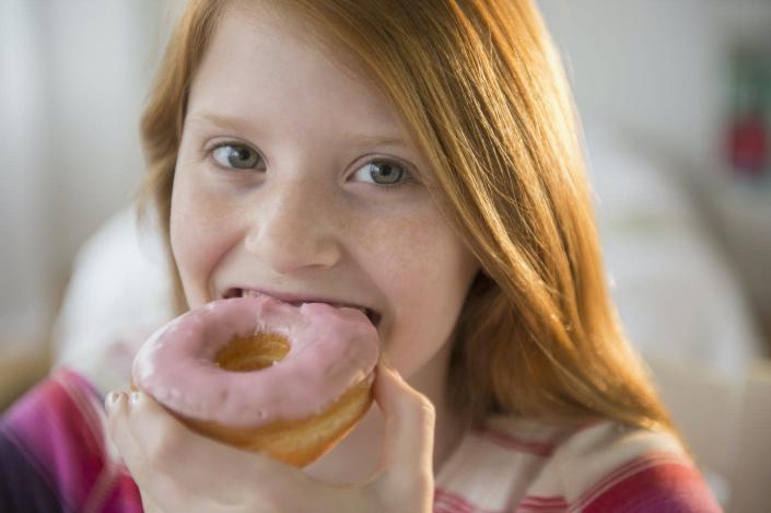 A girl eats a pink glazed donut.