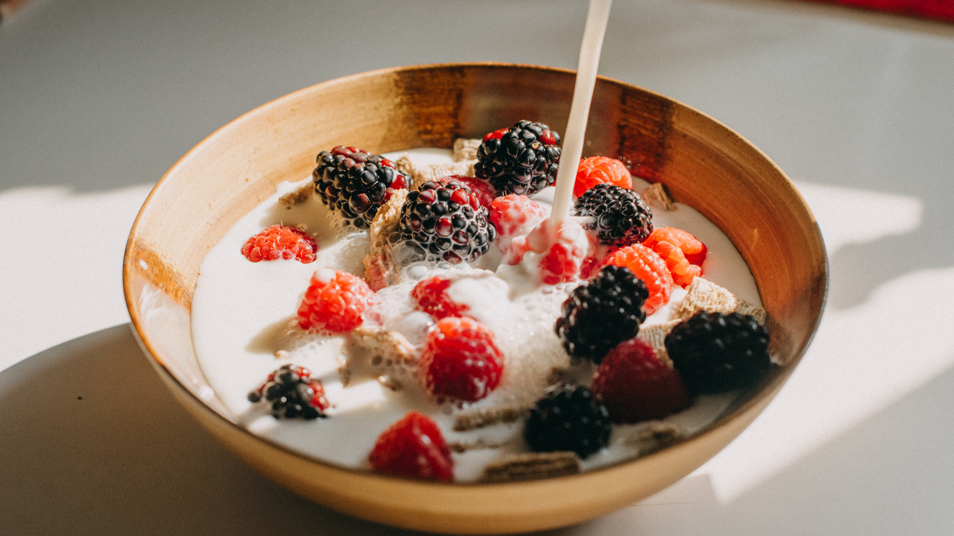 oat milk being poured over cereal and berries