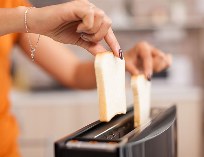 woman placing two slices of white bread in the toaster